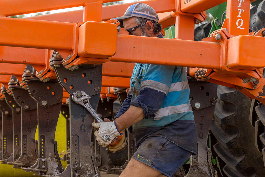 A man is doing maintenance work on a red machine. He is tightening bolts.