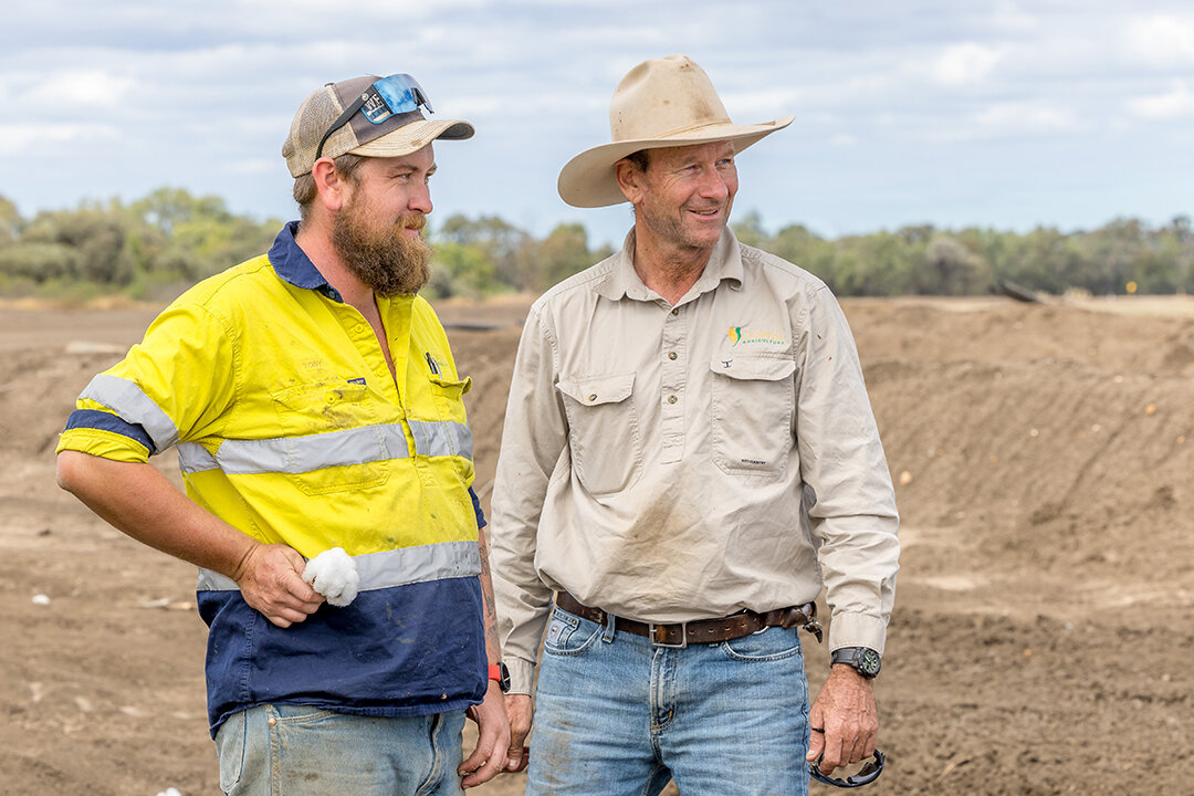 Two men standing together in a dirt area. One is wearing a cowboy hat and Cowal Ag shirt, the other is in a Hi-Viz jacket.